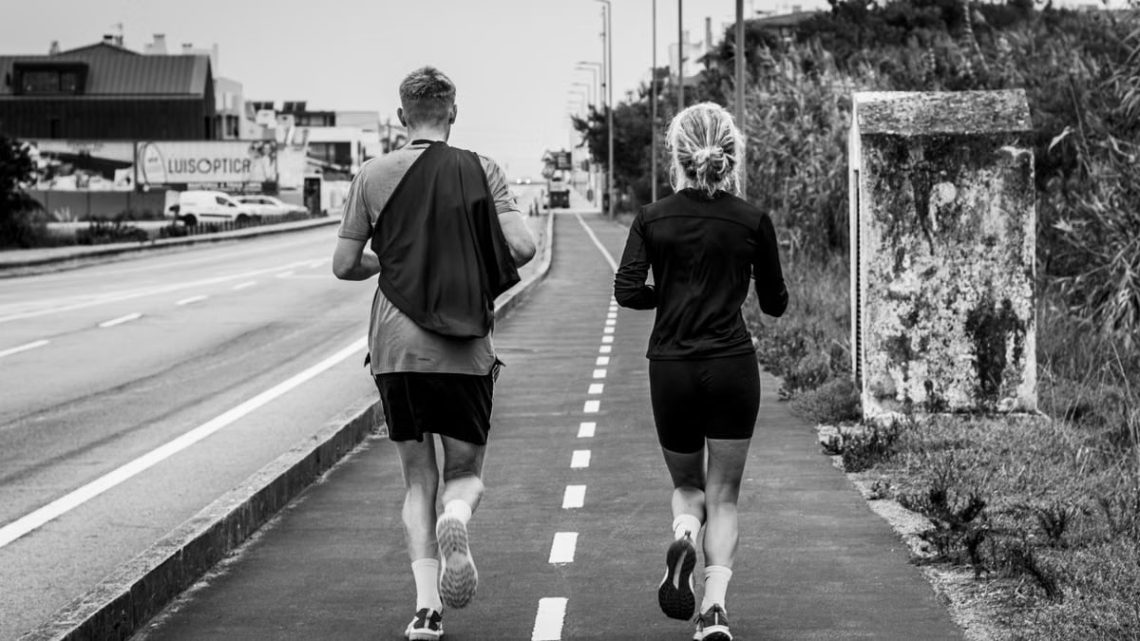 Monochrome photo of two adults jogging on an urban path, showcasing fitness and lifestyle.